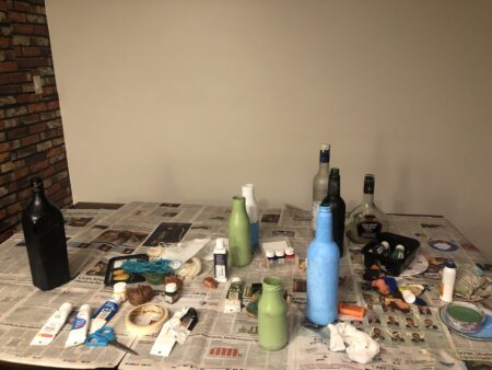 Art supplies and bottles arranged on a table covered with newspapers.