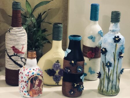 Decorative bottles wrapped in yarn with floral and butterfly designs.